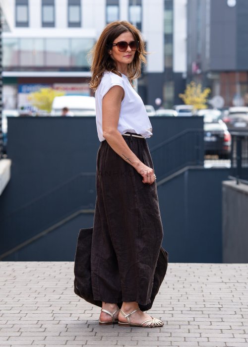 Ciemnobrązowe lniane spodnie damskie z szeroką nogawką i elastycznym pasem ze sznurkiem. Stylizacja casual z białą bluzką i sandałami.