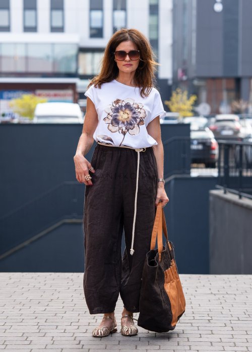 Ciemnobrązowe lniane spodnie damskie z szeroką nogawką i elastycznym pasem ze sznurkiem. Stylizacja casual z białą bluzką i sandałami.