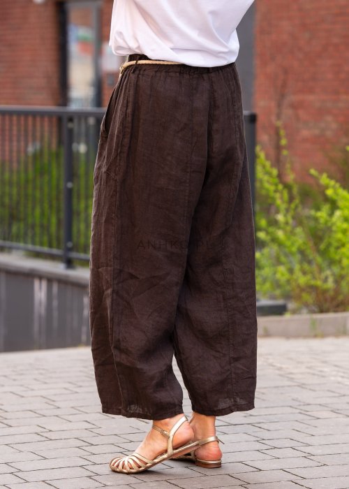Ciemnobrązowe lniane spodnie damskie z szeroką nogawką i elastycznym pasem ze sznurkiem. Stylizacja casual z białą bluzką i sandałami.
