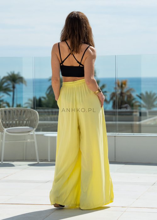 Żółte spodnie damskie z szeroką, lejącą nogawką i elastycznym pasem, stylizowane z czarnym topem w nowoczesnym, miejskim stylu.