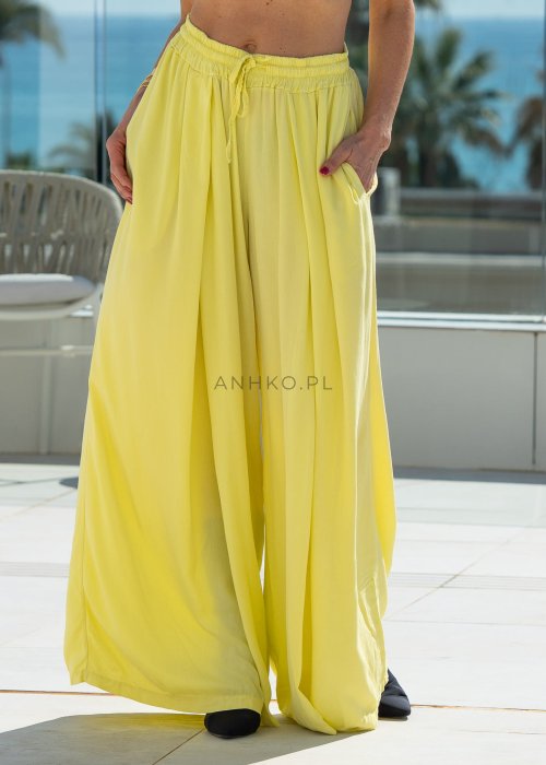 Żółte spodnie damskie z szeroką, lejącą nogawką i elastycznym pasem, stylizowane z czarnym topem w nowoczesnym, miejskim stylu.