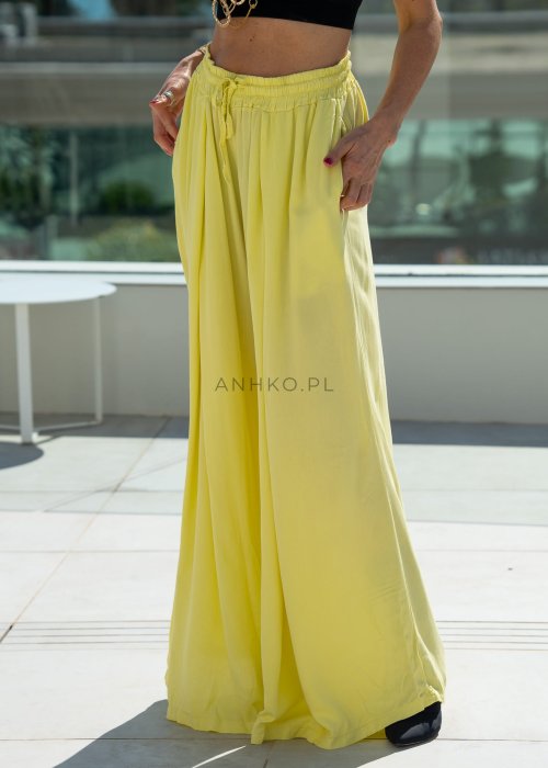 Żółte spodnie damskie z szeroką, lejącą nogawką i elastycznym pasem, stylizowane z czarnym topem w nowoczesnym, miejskim stylu.