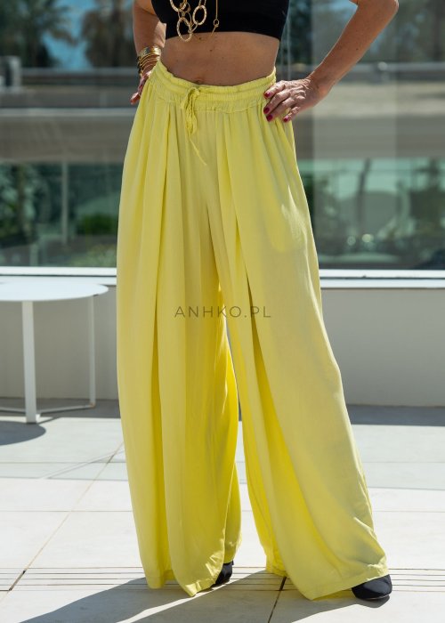 Żółte spodnie damskie z szeroką, lejącą nogawką i elastycznym pasem, stylizowane z czarnym topem w nowoczesnym, miejskim stylu.