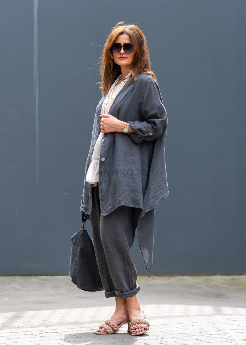 Antracytowa lniana marynarka damska o asymetrycznym kroju z klasycznym kołnierzem i podwijanymi rękawami. Model pokazany w stylizacji z jasną bluzką i lnianymi spodniami.