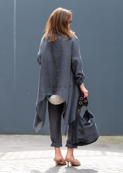 Antracytowa lniana marynarka damska o asymetrycznym kroju z klasycznym kołnierzem i podwijanymi rękawami. Model pokazany w stylizacji z jasną bluzką i lnianymi spodniami.