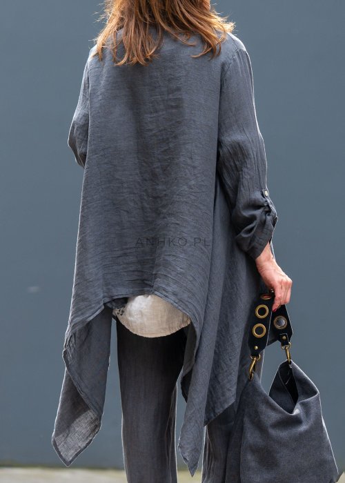 Antracytowa lniana marynarka damska o asymetrycznym kroju z klasycznym kołnierzem i podwijanymi rękawami. Model pokazany w stylizacji z jasną bluzką i lnianymi spodniami.