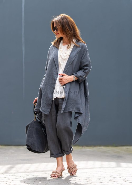 Antracytowa lniana marynarka damska o asymetrycznym kroju z klasycznym kołnierzem i podwijanymi rękawami. Model pokazany w stylizacji z jasną bluzką i lnianymi spodniami.