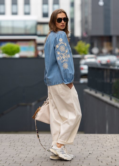 Śmietankowe spodnie damskie o luźnym kroju boyfriend z elastycznym pasem i troczkiem, zestawione ze sneakersami. Model ma podwijane nogawki i praktyczne kieszenie, tworząc swobodną stylizację miejską.