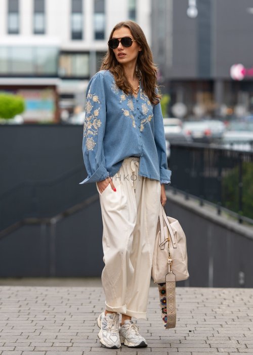 Śmietankowe spodnie damskie o luźnym kroju boyfriend z elastycznym pasem i troczkiem, zestawione ze sneakersami. Model ma podwijane nogawki i praktyczne kieszenie, tworząc swobodną stylizację miejską.