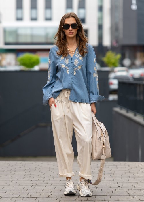 Śmietankowe spodnie damskie o luźnym kroju boyfriend z elastycznym pasem i troczkiem, zestawione ze sneakersami. Model ma podwijane nogawki i praktyczne kieszenie, tworząc swobodną stylizację miejską.