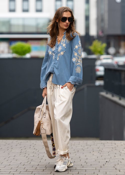 Śmietankowe spodnie damskie o luźnym kroju boyfriend z elastycznym pasem i troczkiem, zestawione ze sneakersami. Model ma podwijane nogawki i praktyczne kieszenie, tworząc swobodną stylizację miejską.