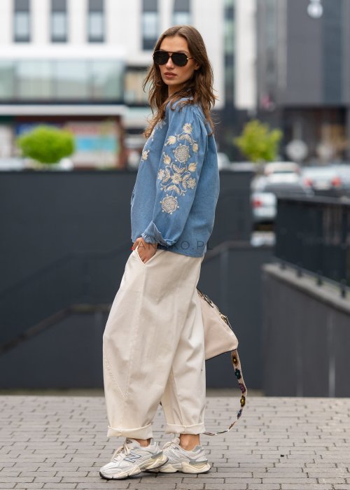 Śmietankowe spodnie damskie o luźnym kroju boyfriend z elastycznym pasem i troczkiem, zestawione ze sneakersami. Model ma podwijane nogawki i praktyczne kieszenie, tworząc swobodną stylizację miejską.