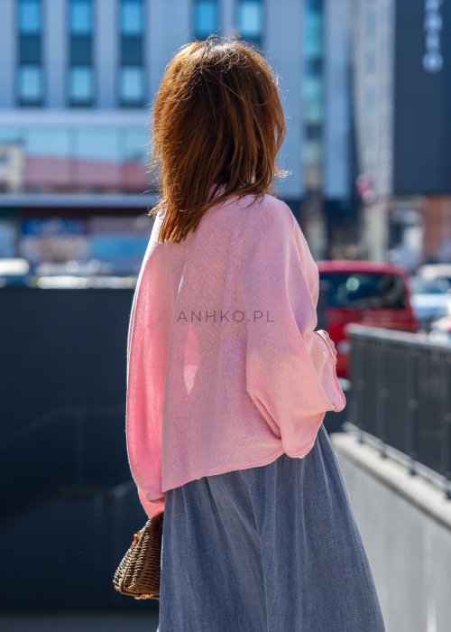 Jasnoróżowy sweter oversize z bawełnianej dzianiny i asymetrycznym dołem, zestawiony z długą szarą spódnicą w eleganckiej miejskiej stylizacji.