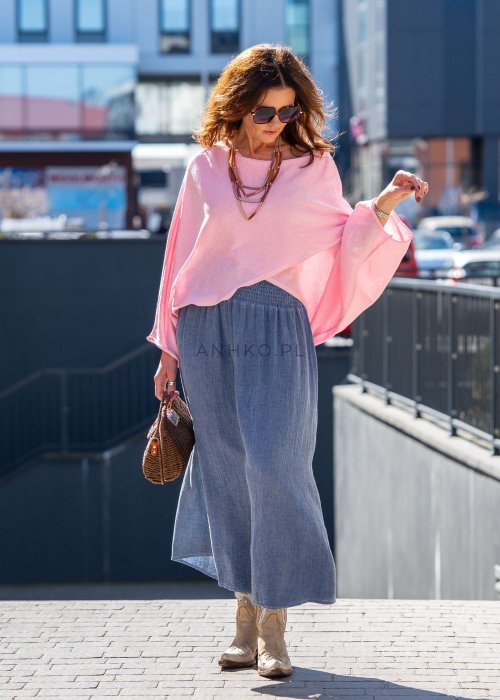 Jasnoróżowy sweter oversize z bawełnianej dzianiny i asymetrycznym dołem, zestawiony z długą szarą spódnicą w eleganckiej miejskiej stylizacji.