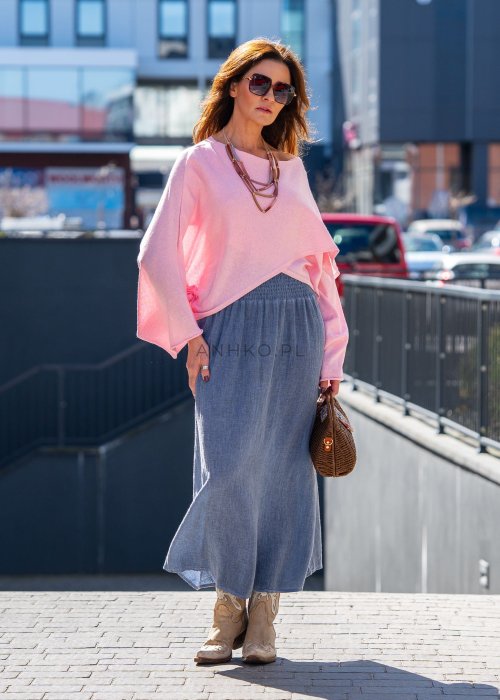 Jasnoróżowy sweter oversize z bawełnianej dzianiny i asymetrycznym dołem, zestawiony z długą szarą spódnicą w eleganckiej miejskiej stylizacji.