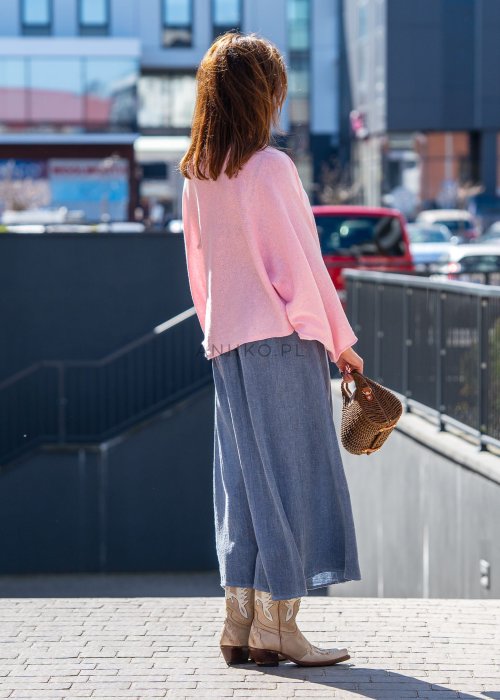 Jasnoróżowy sweter oversize z bawełnianej dzianiny i asymetrycznym dołem, zestawiony z długą szarą spódnicą w eleganckiej miejskiej stylizacji.