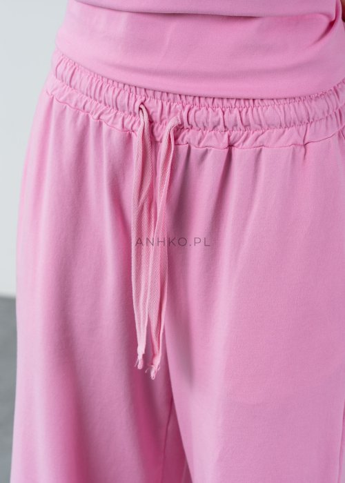 Różowe spodnie dresowe damskie z elastyczną talią i sznurkiem, o luźnym kroju i długich nogawkach, stylizowane w miejskim casualowym looku ze sneakersami.