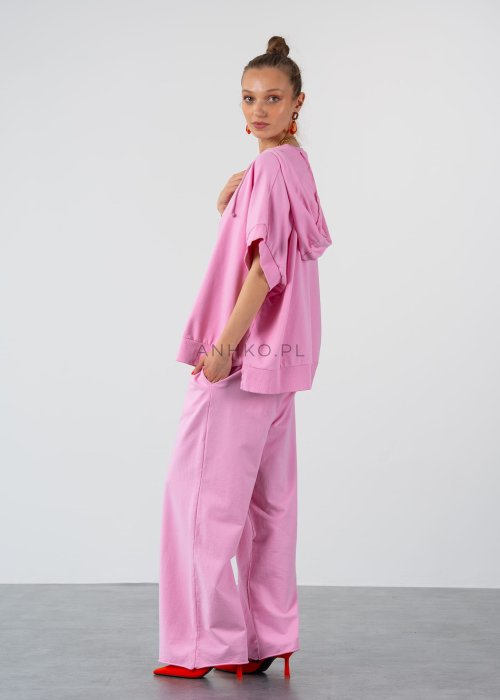 Różowe spodnie dresowe damskie z elastyczną talią i sznurkiem, o luźnym kroju i długich nogawkach, stylizowane w miejskim casualowym looku ze sneakersami.