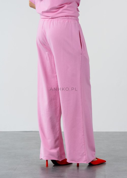 Różowe spodnie dresowe damskie z elastyczną talią i sznurkiem, o luźnym kroju i długich nogawkach, stylizowane w miejskim casualowym looku ze sneakersami.