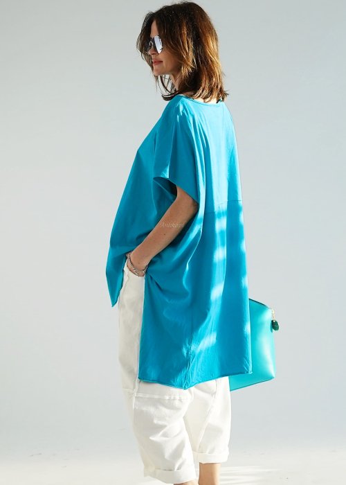 Turkusowa bluzka oversize z asymetrycznym dołem i wydłużonym tyłem, zestawiona z jasnymi spodniami. Luźny fason tworzy świeżą, nowoczesną stylizację.