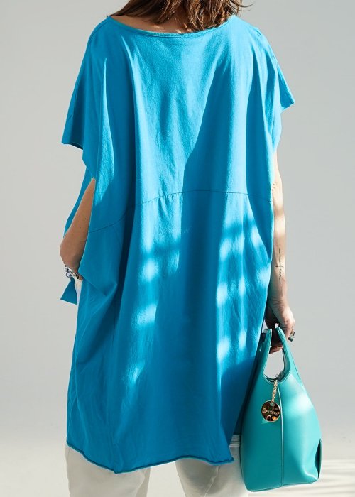 Turkusowa bluzka oversize z asymetrycznym dołem i wydłużonym tyłem, zestawiona z jasnymi spodniami. Luźny fason tworzy świeżą, nowoczesną stylizację.