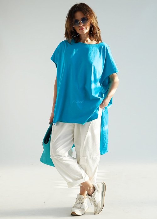 Turkusowa bluzka oversize z asymetrycznym dołem i wydłużonym tyłem, zestawiona z jasnymi spodniami. Luźny fason tworzy świeżą, nowoczesną stylizację.