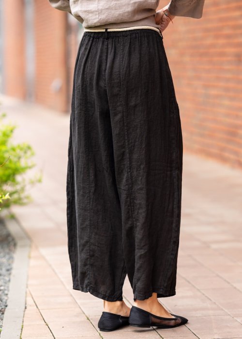 Czarne lniane spodnie damskie z szeroką nogawką i elastycznym pasem ze sznurkiem. Stylizacja casual z lekką bluzką i balerinami w miejskim wydaniu.