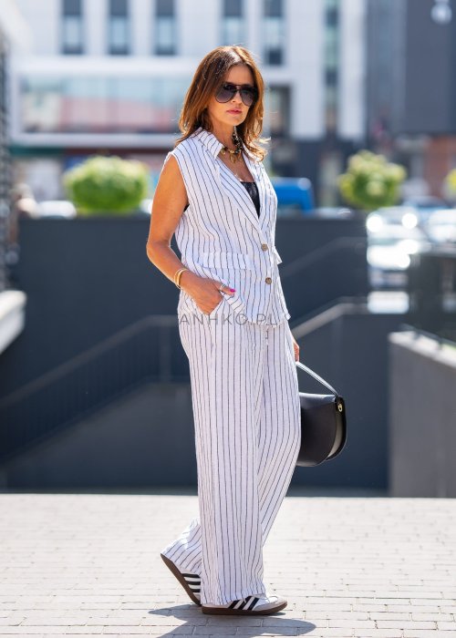 Biała kamizelka lniana damska w pionowe paski z klapami i zapięciem na dwa guziki, zestawiona z szerokimi spodniami w komplecie. Elegancka stylizacja miejska z lekką kamizelką bez rękawów.