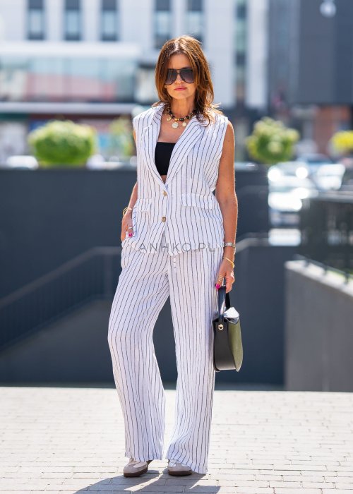 Biała kamizelka lniana damska w pionowe paski z klapami i zapięciem na dwa guziki, zestawiona z szerokimi spodniami w komplecie. Elegancka stylizacja miejska z lekką kamizelką bez rękawów.