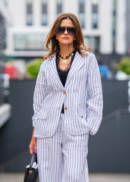 Lniana marynarka damska w białym kolorze w pionowe paski z klasycznymi klapami i drewnianymi guzikami. Stylizacja elegancka z miejskim charakterem.