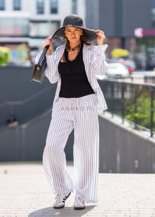 Lniana marynarka damska w białym kolorze w pionowe paski z klasycznymi klapami i drewnianymi guzikami. Stylizacja elegancka z miejskim charakterem.