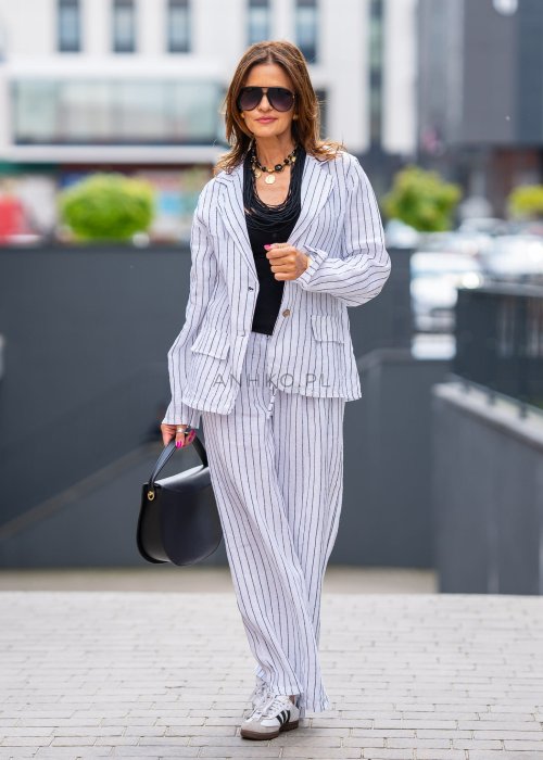 Lniana marynarka damska w białym kolorze w pionowe paski z klasycznymi klapami i drewnianymi guzikami. Stylizacja elegancka z miejskim charakterem.