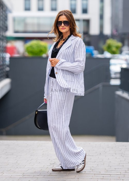 Lniana marynarka damska w białym kolorze w pionowe paski z klasycznymi klapami i drewnianymi guzikami. Stylizacja elegancka z miejskim charakterem.