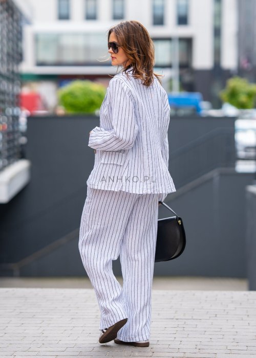 Lniana marynarka damska w białym kolorze w pionowe paski z klasycznymi klapami i drewnianymi guzikami. Stylizacja elegancka z miejskim charakterem.