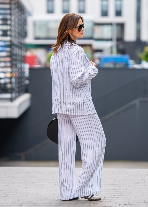 Lniana marynarka damska w białym kolorze w pionowe paski z klasycznymi klapami i drewnianymi guzikami. Stylizacja elegancka z miejskim charakterem.