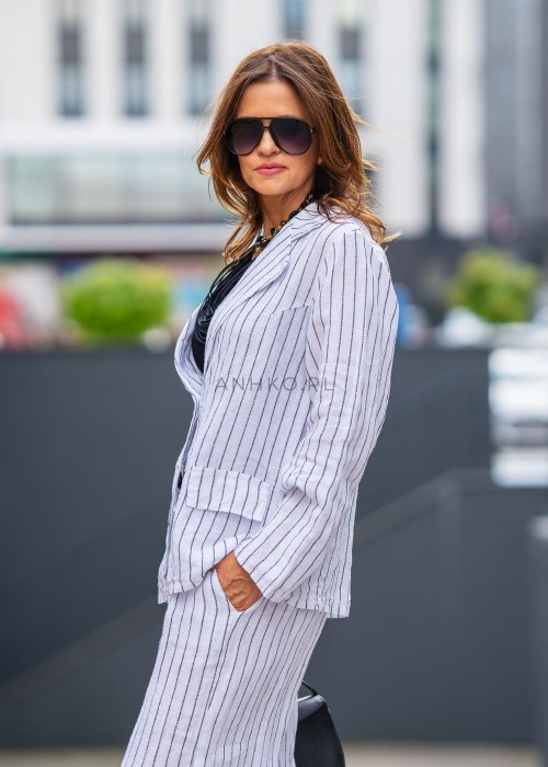 Lniana marynarka damska w białym kolorze w pionowe paski z klasycznymi klapami i drewnianymi guzikami. Stylizacja elegancka z miejskim charakterem.
