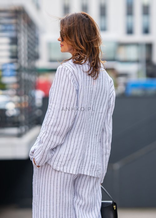 Lniana marynarka damska w białym kolorze w pionowe paski z klasycznymi klapami i drewnianymi guzikami. Stylizacja elegancka z miejskim charakterem.