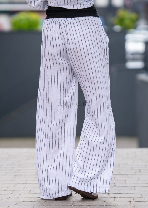 Spodnie lniane damskie w białym kolorze w pionowe paski z szerokimi nogawkami i elastycznym pasem. Stylizacja lekka i elegancka.