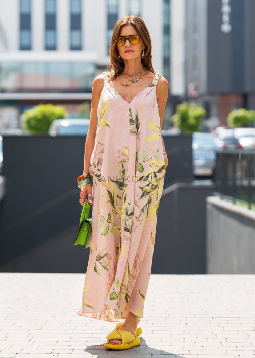 Jasnoróżowa damska sukienka lniana maxi z roślinnym printem i marszczonymi ramiączkami. Lekka, luźna forma z kieszeniami, prezentowana w miejskiej stylizacji.