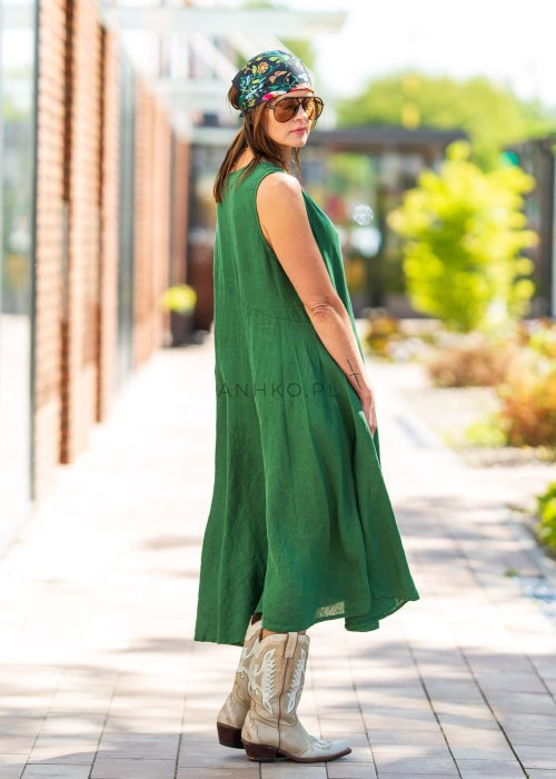 Zielona lniana sukienka maxi bez rękawów o luźnym fasonie z asymetrycznym dołem, stylizowana z kowbojkami i dużą torbą.