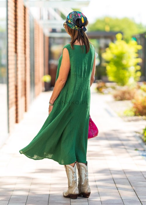 Zielona lniana sukienka maxi bez rękawów o luźnym fasonie z asymetrycznym dołem, stylizowana z kowbojkami i dużą torbą.