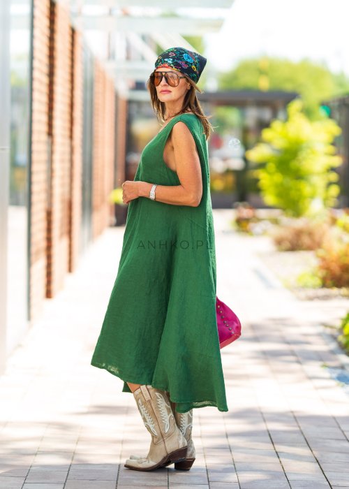 Zielona lniana sukienka maxi bez rękawów o luźnym fasonie z asymetrycznym dołem, stylizowana z kowbojkami i dużą torbą.