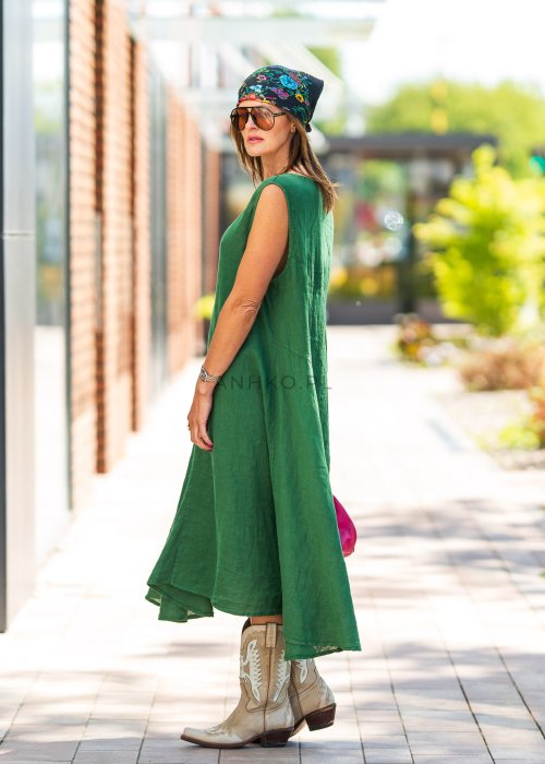Zielona lniana sukienka maxi bez rękawów o luźnym fasonie z asymetrycznym dołem, stylizowana z kowbojkami i dużą torbą.