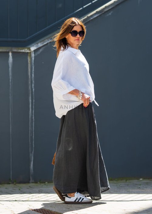 Biała koszula lniana damska o luźnym kroju z kołnierzykiem i kieszonką, zestawiona z czarną spódnicą i minimalistyczną biżuterią w eleganckim stylu.