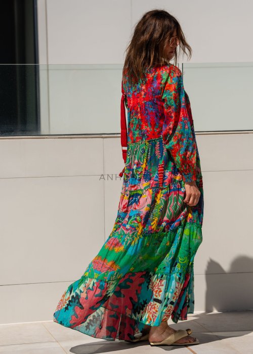 Długa sukienka maxi Ontario Neo Multicolor z roślinnym printem, falbanami i guzikami z przodu. Stylizacja z czerwoną torebką i sandałami.