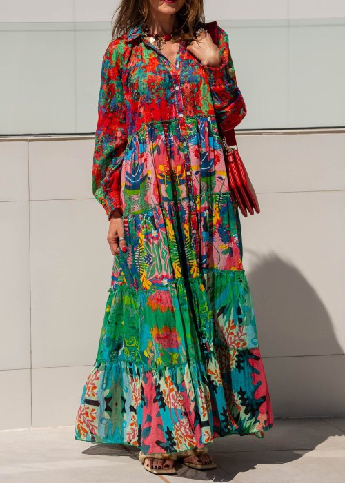 Długa sukienka maxi Ontario Neo Multicolor z roślinnym printem, falbanami i guzikami z przodu. Stylizacja z czerwoną torebką i sandałami.