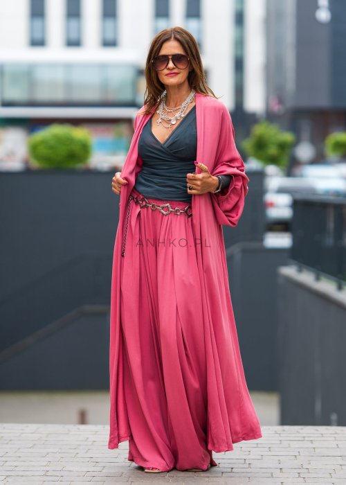 Różowe kimono damskie maxi z długim, płynnie układającym się fasonem i bufiastymi rękawami. Model pokazany w stylizacji z topem i szerokimi spodniami, w nowoczesnym miejskim wydaniu.