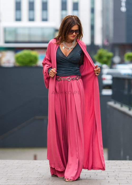 Różowe kimono damskie maxi z długim, płynnie układającym się fasonem i bufiastymi rękawami. Model pokazany w stylizacji z topem i szerokimi spodniami, w nowoczesnym miejskim wydaniu.