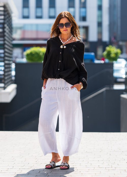 Czarna lniana koszula damska oversize z dekoltem V i guzikami, zestawiona z jasnymi spodniami w eleganckiej, miejskiej stylizacji.