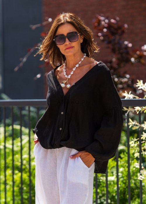 Czarna lniana koszula damska oversize z dekoltem V i guzikami, zestawiona z jasnymi spodniami w eleganckiej, miejskiej stylizacji.